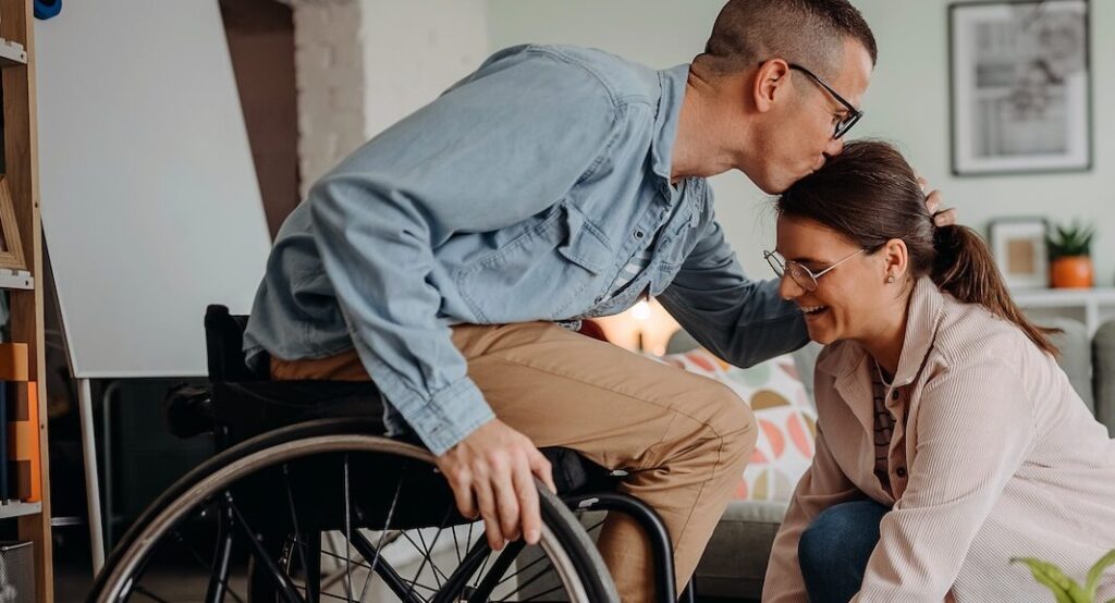 Person in Wheelcare kissing partner on forehead aspect ratio 850 460